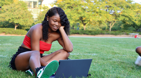 Student sitting outside in the presidents courtyard in summer working on their laptop